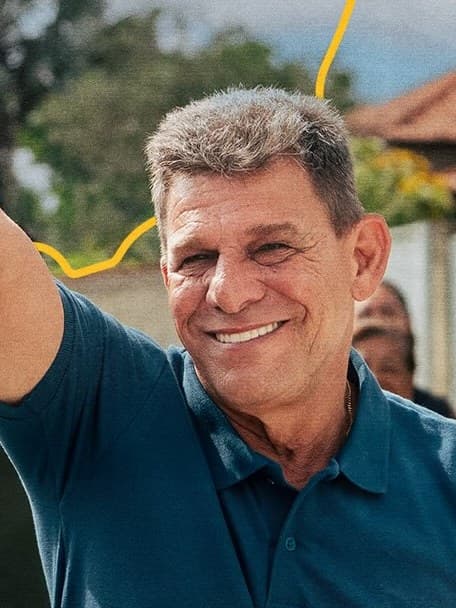 Carlos Russo sorri e levanta o polegar em uma rua de Araruama, acompanhado de moradores